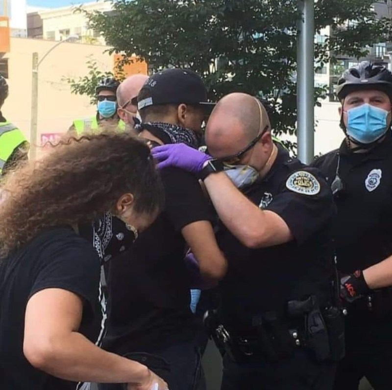 Police officer prays with a young black man. 
