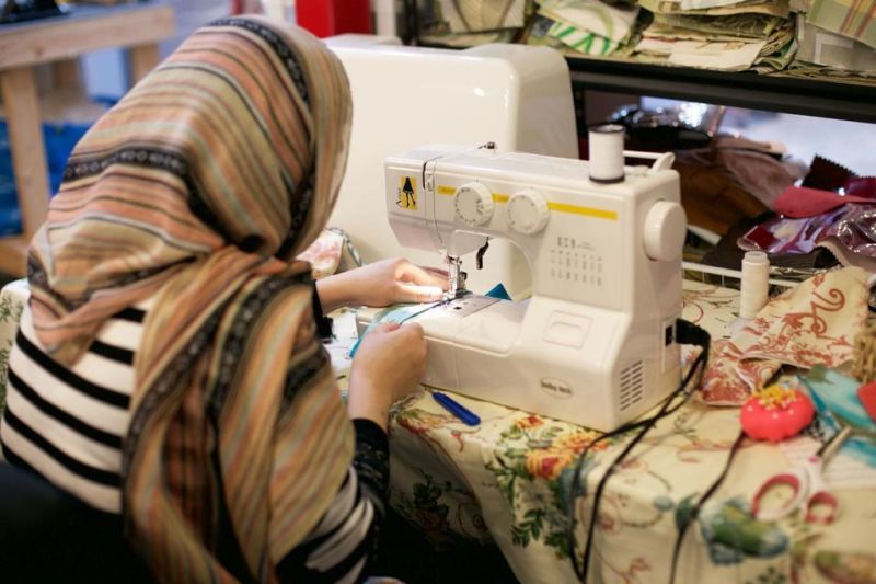 photo of refugee working with a sewing machine on a project.Peace of Thread