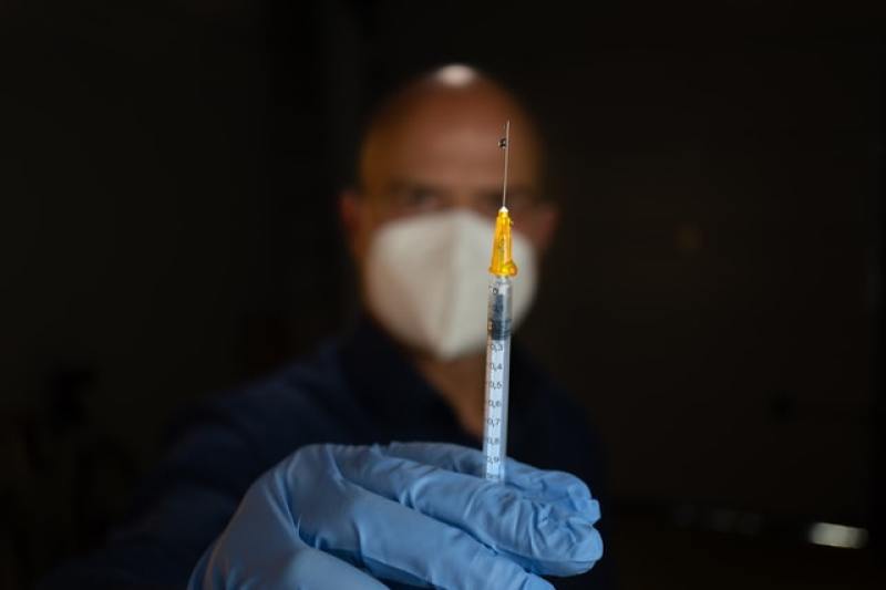 syringe held in hand by man wearing mask and gloves