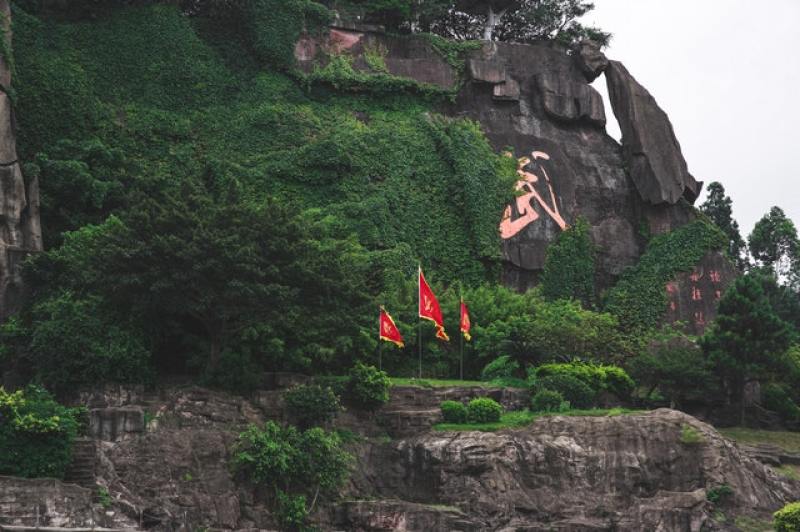 rock wall / mountain face with a huge Chinese letter inscribed on it and red flags in front