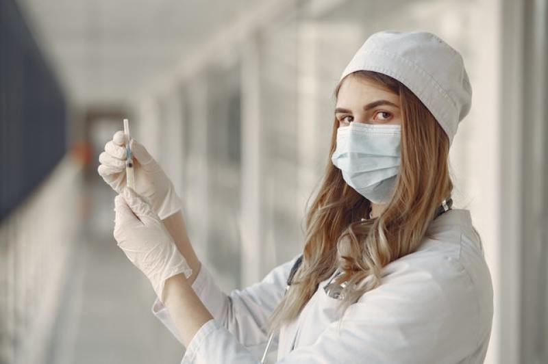 woman doctor in medical garb and mask holding an injection