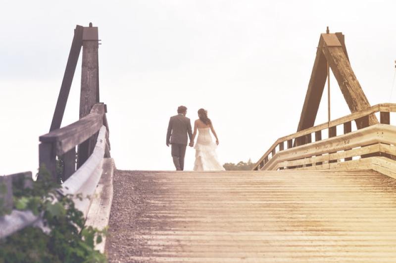 newlywed couple walking hand in hand on bridge