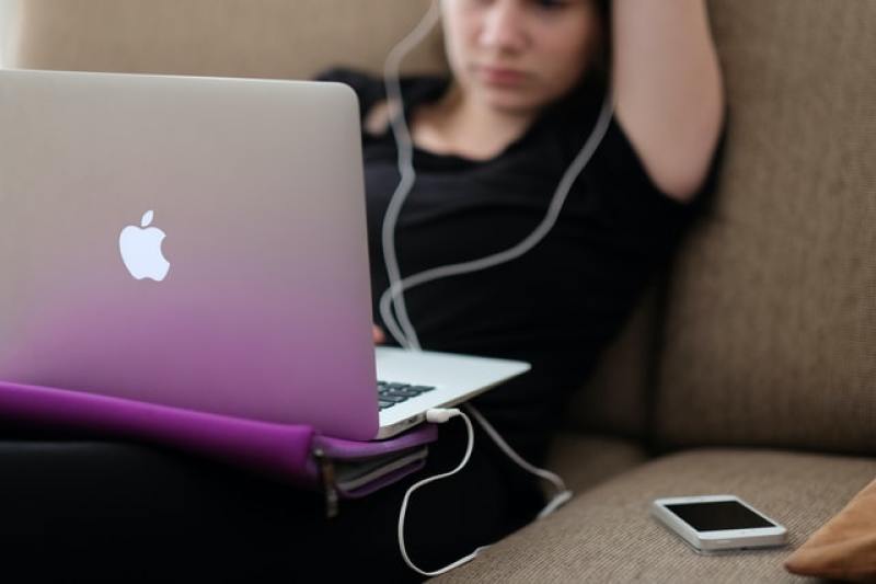 teen watching on a macbook beside her phone