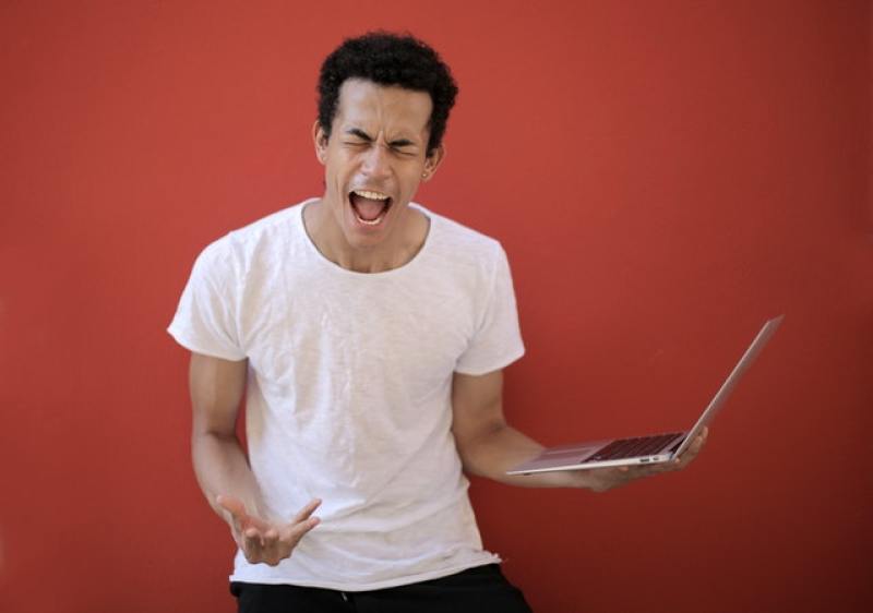 angry man screaming while holding a laptop