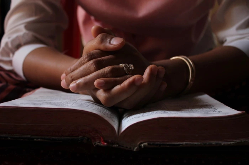 Hands in Prayer Placed on the Bible